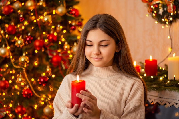 Petite fille avec une bougie allumée près de l'arbre de Noël Faire un concept de souhait célébrant Noël