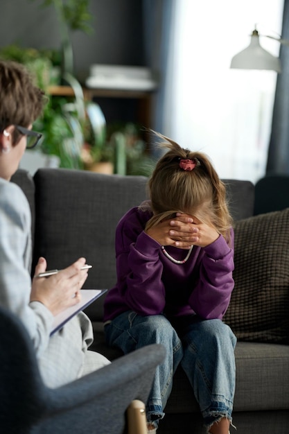 Petite fille bouleversée assise sur un canapé de mauvaise humeur pendant que le psychologue lui parle pendant leur réunion