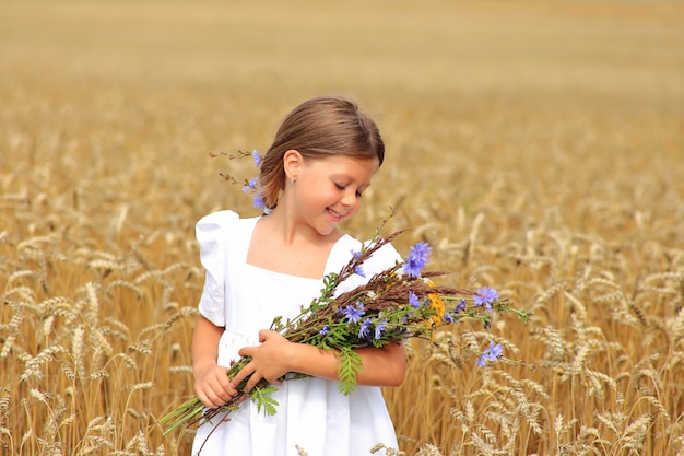 Petite fille avec un bouquet de fleurs sauvages dans ses mains dans un champ de blé.