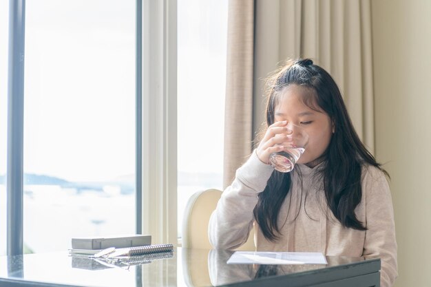 Petite fille buvant de l'eau assise sur une chaise à la maison, concept de santé et de soins