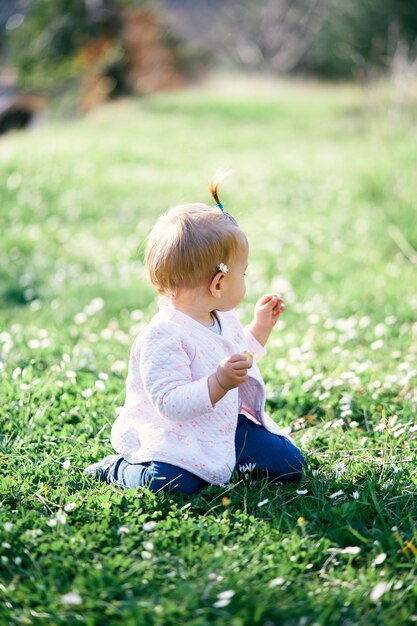 Petite fille avec une camomille derrière son oreille est assise sur une pelouse verte vue arrière