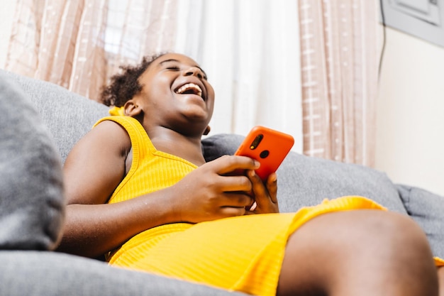 Petite fille sur un canapé en riant à l'aide d'un smartphone à la recherche d'un mème