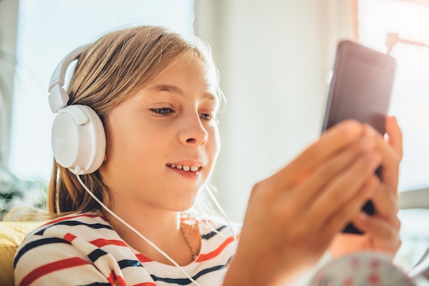 Petite fille avec un casque à l'aide de téléphone intelligent