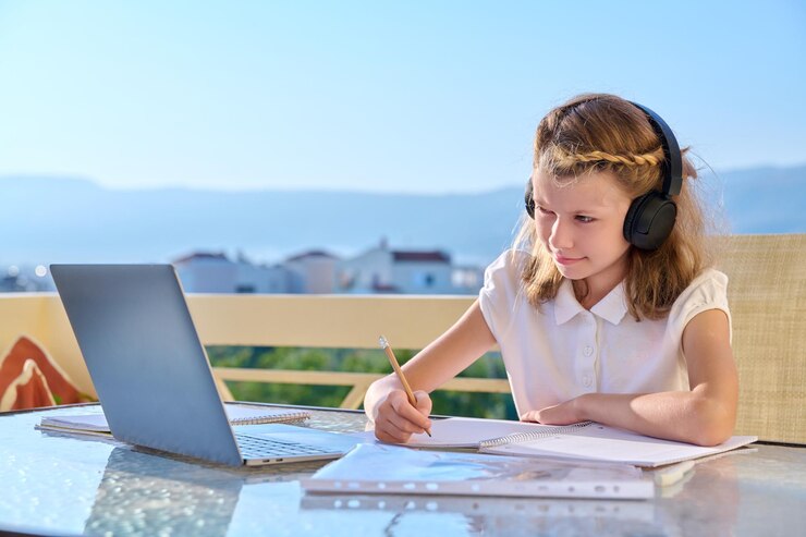 Une petite fille avec un casque étudie à l'aide d'un ordinateur portable