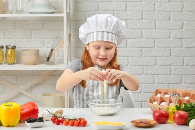 La petite fille casse l'oeuf jaune en pâte fraîche