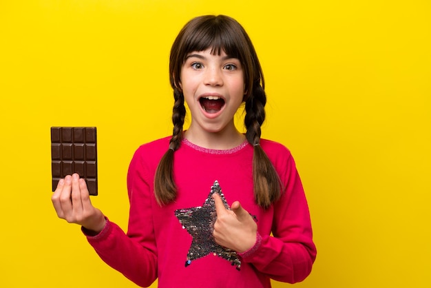 Petite fille caucasienne au chocolat isolée sur fond jaune avec une expression faciale surprise