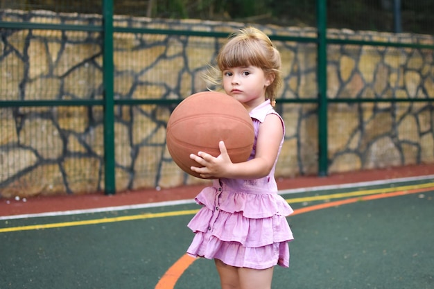 petite fille caucasienne avec ballon sur aire de jeux extérieure sports pour enfants pour la santé