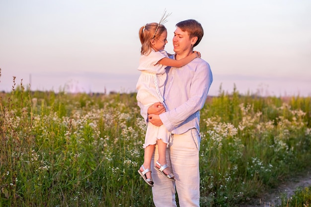 Petite fille caucasienne dans les bras de son père sur le terrain à l'heure d'été du coucher du soleil.