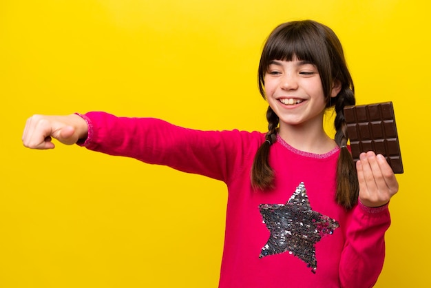 Petite fille caucasienne avec du chocolat isolé sur fond jaune donnant un geste du pouce levé