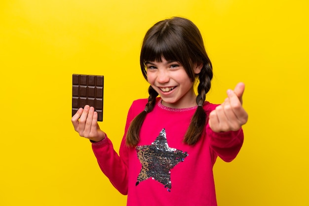 Petite fille caucasienne avec du chocolat isolé sur fond jaune faisant un geste d'argent