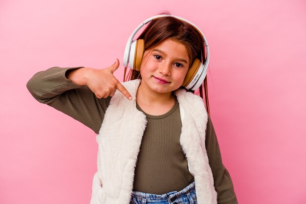 Petite Fille Caucasienne écoute De La Musique Isolée Sur Mur Rose Personne Pointant à La Main Vers Un Espace De Copie De Chemise, Fier Et Confiant