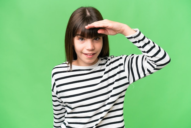 Petite fille caucasienne sur fond isolé regardant loin avec la main pour regarder quelque chose