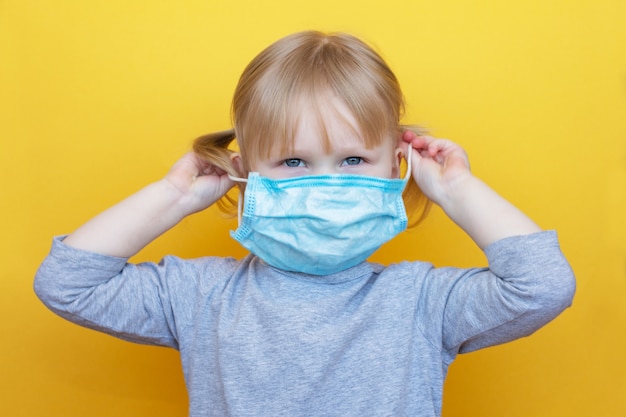 Petite fille caucasienne habille un masque de protection sur backgraund jaune