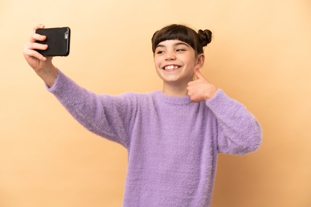 Petite fille caucasienne isolée sur beige faisant un selfie avec téléphone mobile