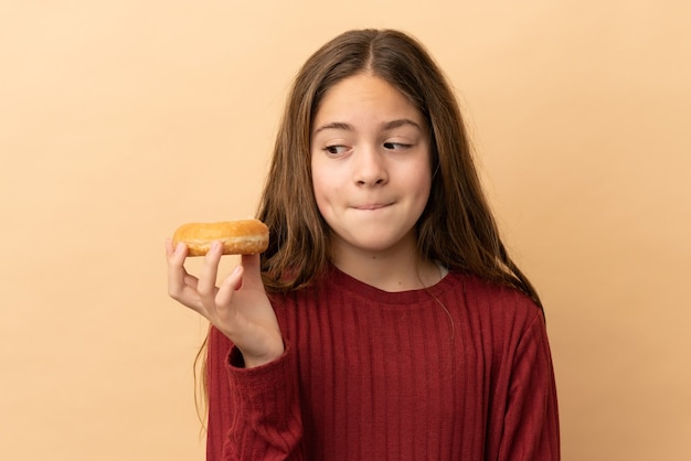 Petite fille caucasienne isolée sur fond beige tenant un beignet