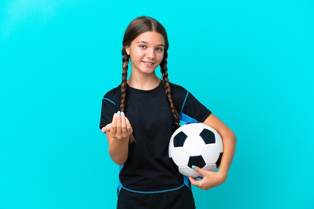 Petite fille caucasienne isolée sur fond bleu avec ballon de football et faisant un geste à venir