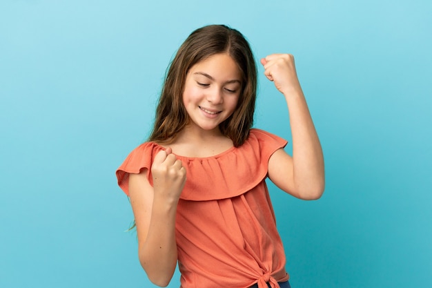 Petite fille caucasienne isolée sur fond bleu célébrant une victoire