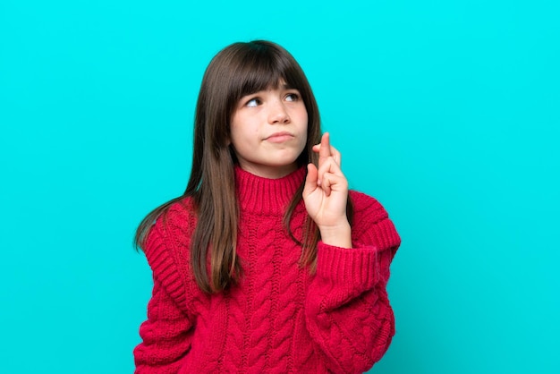 Petite fille caucasienne isolée sur fond bleu avec les doigts croisés et souhaitant le meilleur