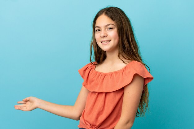 Petite fille caucasienne isolée sur fond bleu étendant les mains sur le côté pour inviter à venir