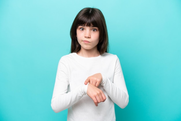 Petite fille caucasienne isolée sur fond bleu faisant le geste d'être en retard