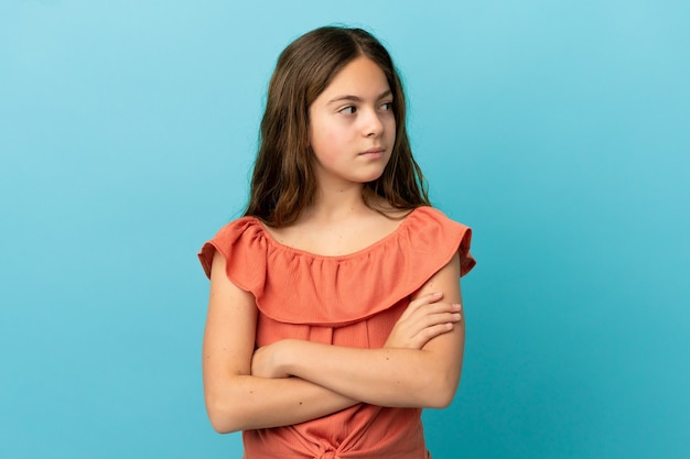 Petite fille caucasienne isolée sur fond bleu en gardant les bras croisés