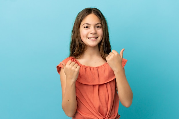 Petite fille caucasienne isolée sur fond bleu avec un geste de pouce levé et souriant