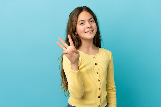 Petite fille caucasienne isolée sur fond bleu heureuse et comptant trois avec les doigts