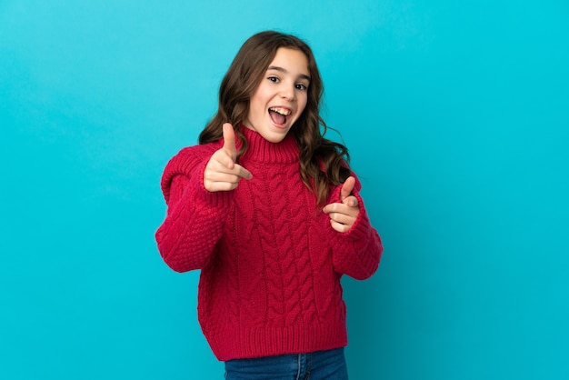 Petite fille caucasienne isolée sur fond bleu pointant vers l'avant et souriant