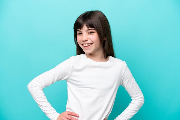 Petite fille caucasienne isolée sur fond bleu posant avec les bras à la hanche et souriant