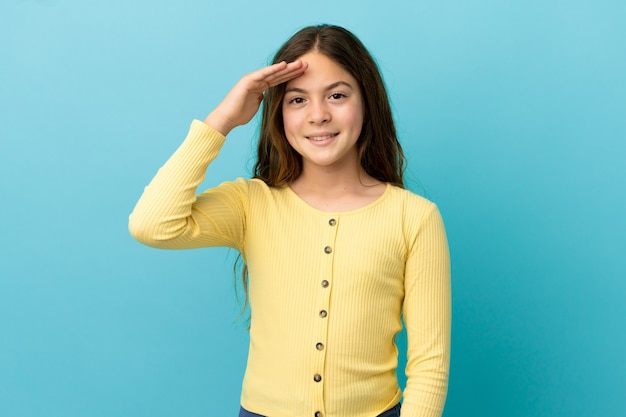 Petite fille caucasienne isolée sur fond bleu saluant avec la main avec une expression heureuse