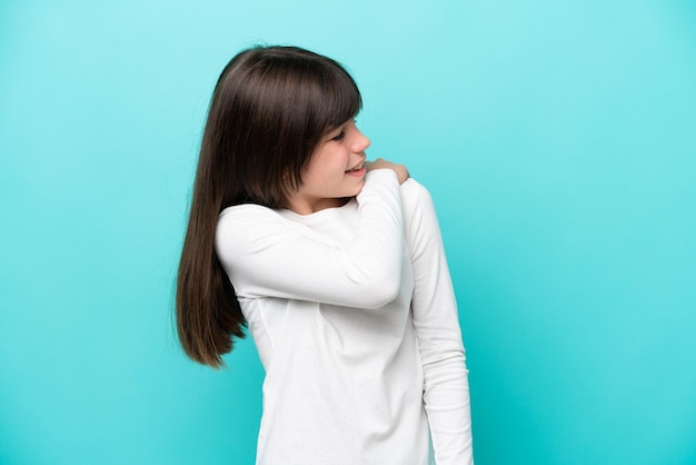 Petite fille caucasienne isolée sur fond bleu souffrant de douleurs à l'épaule pour avoir fait un effort