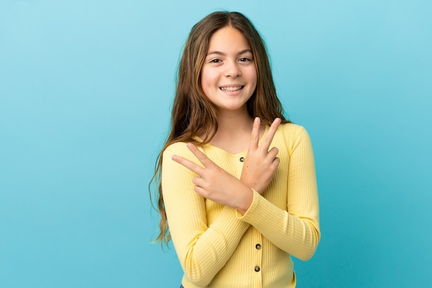 Petite fille caucasienne isolée sur fond bleu souriant et montrant le signe de la victoire