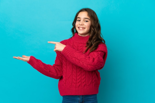 Petite fille caucasienne isolée sur fond bleu tenant un espace de copie imaginaire sur la paume pour insérer une annonce