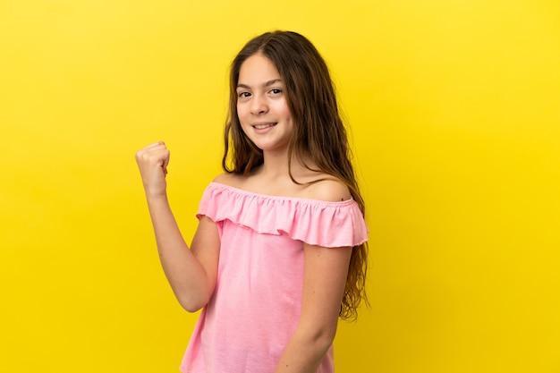 Petite fille caucasienne isolée sur fond jaune célébrant une victoire