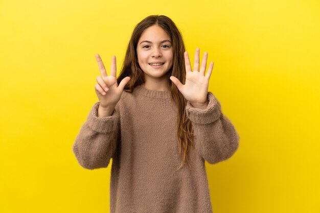 Petite fille caucasienne isolée sur fond jaune comptant huit avec les doigts