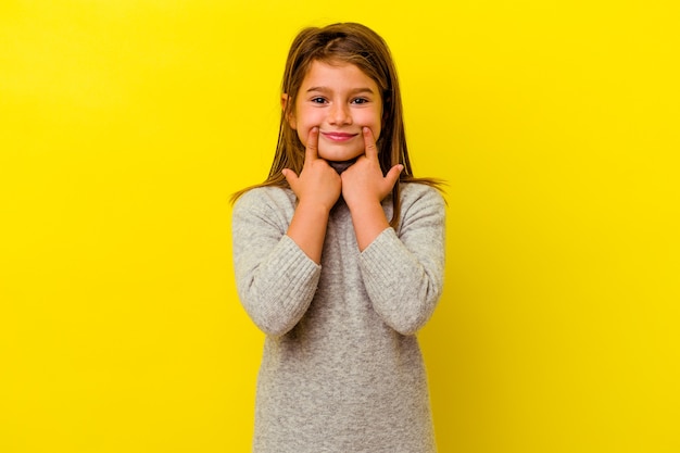 Petite fille caucasienne isolée sur fond jaune doutant entre deux options.