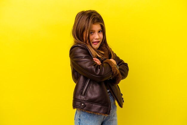 Petite fille caucasienne isolée sur fond jaune drôle et sympathique qui sort la langue.