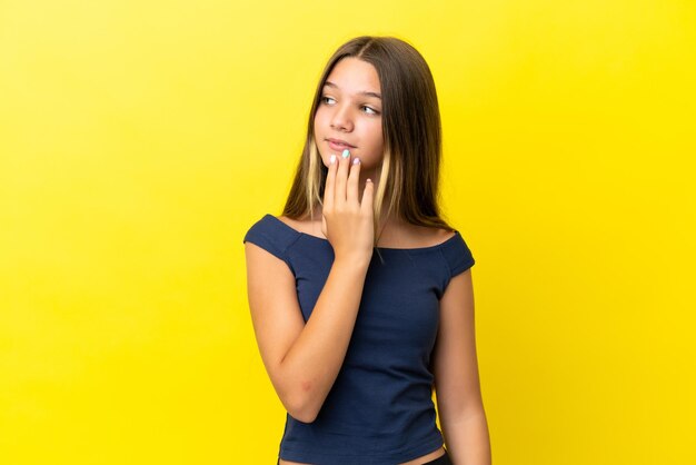 Petite fille caucasienne isolée sur fond jaune en levant tout en souriant