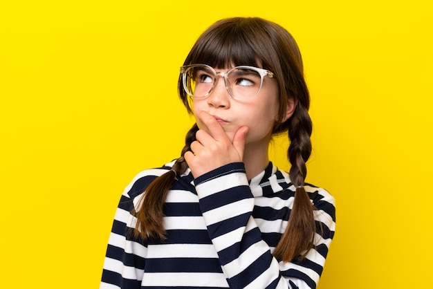 Petite fille caucasienne isolée sur fond jaune avec des lunettes et ayant des doutes