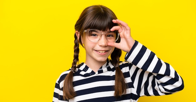 Petite fille caucasienne isolée sur fond jaune avec des lunettes avec une expression heureuse