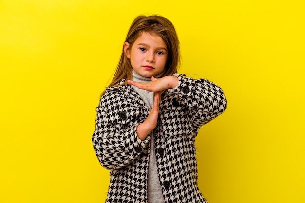 Petite fille caucasienne isolée sur fond jaune montrant un geste de délai d'attente.