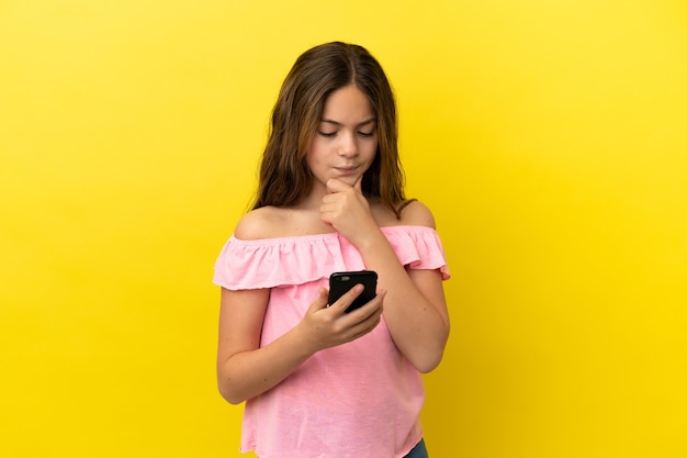 Petite fille caucasienne isolée sur fond jaune pensant et envoyant un message