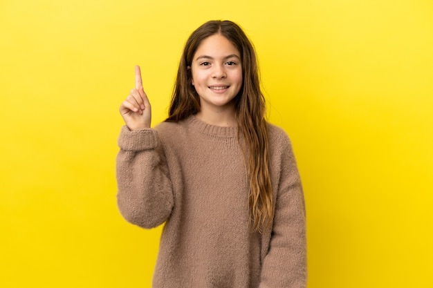 Petite fille caucasienne isolée sur fond jaune pointant vers une excellente idée