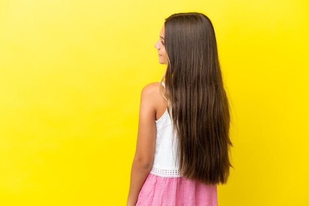 Petite fille caucasienne isolée sur fond jaune en position arrière et regardant de côté