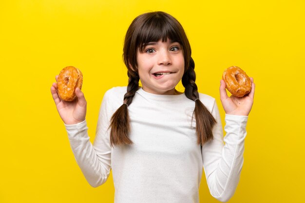 Petite fille caucasienne isolée sur fond jaune tenant des beignets