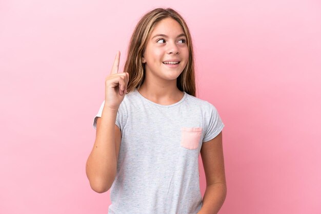 Petite fille caucasienne isolée sur fond rose ayant l'intention de réaliser la solution tout en levant un doigt