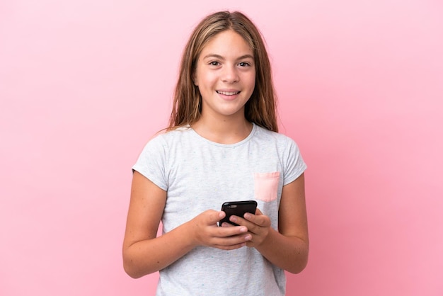 Petite fille caucasienne isolée sur fond rose envoyant un message avec le mobile