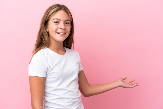 Petite fille caucasienne isolée sur fond rose étendant les mains sur le côté pour inviter à venir