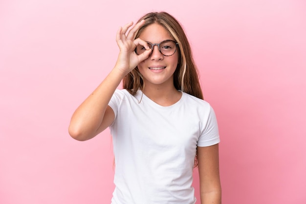 Petite fille caucasienne isolée sur fond rose avec des lunettes avec une expression heureuse