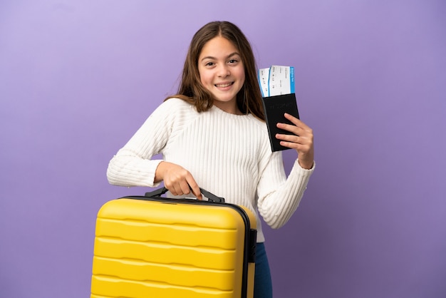 Petite fille caucasienne isolée sur fond violet en vacances avec valise et passeport